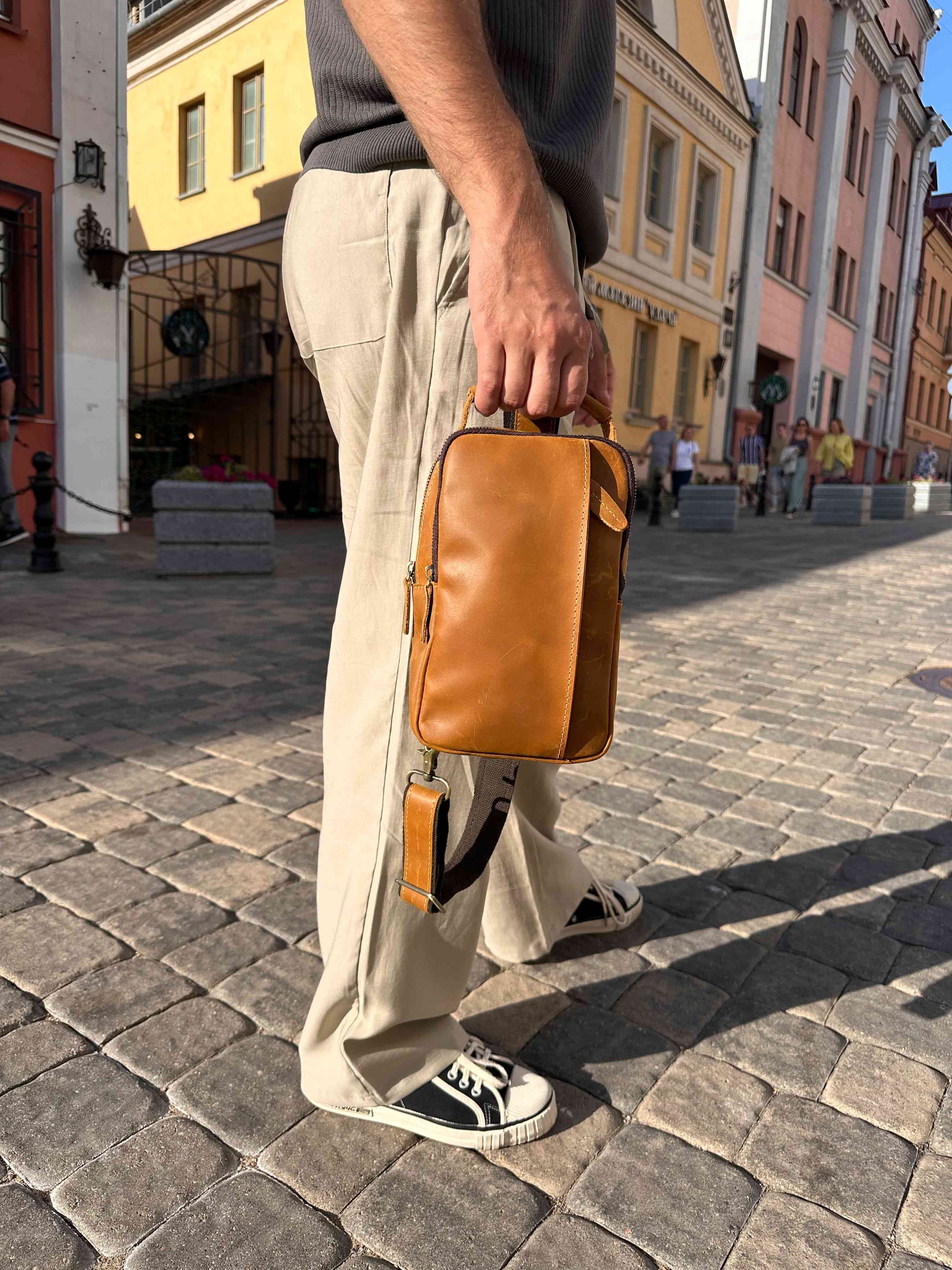 Brown leather crossbody sling bag carried by hand, stylish compact bag for travel and city use