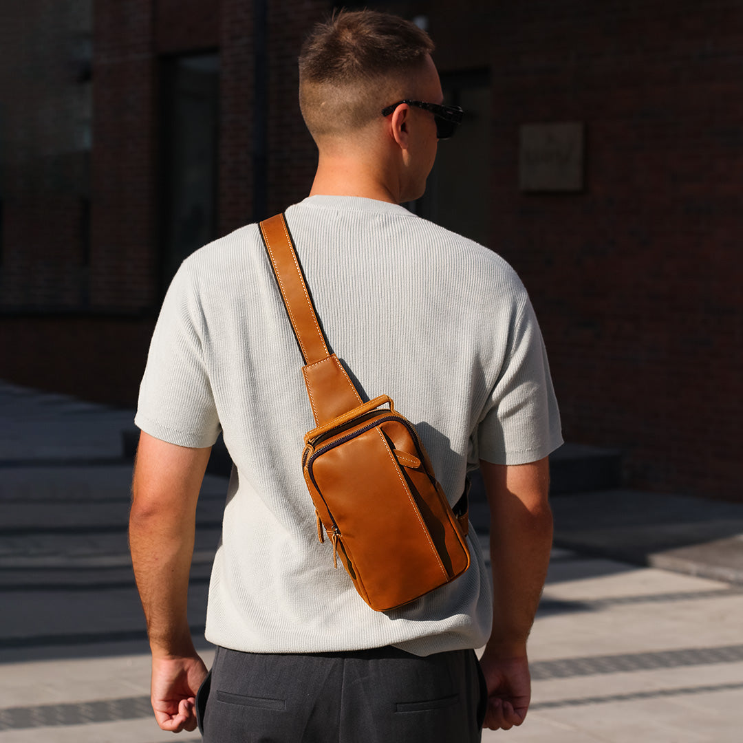 Tan leather crossbody sling bag worn on the back by man, stylish everyday use bag