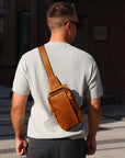 Tan leather crossbody sling bag worn on the back by man, stylish everyday use bag
