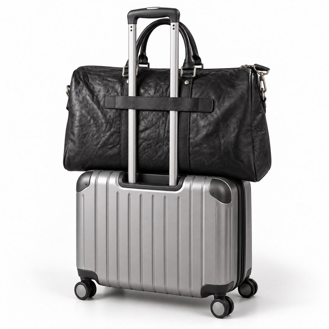 Textured black full-grain leather weekender bag secured to a rolling suitcase with its trolley sleeve.