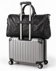 Textured black full-grain leather weekender bag secured to a rolling suitcase with its trolley sleeve.