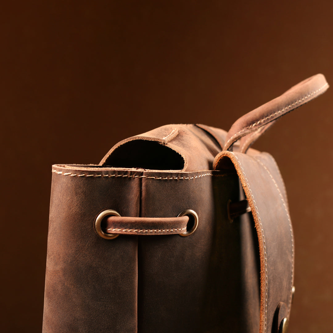 Close-up of the top handle and opening of a vintage brown leather backpack, showcasing Crazy Horse leather and stitching.