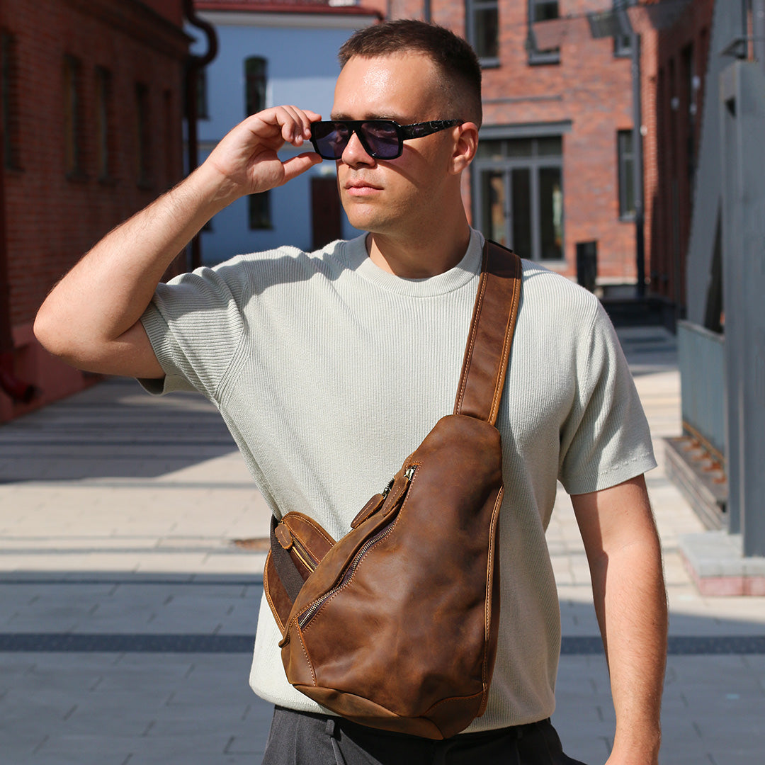 Man wearing sunglasses and a brown leather sling bag in an urban setting