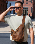 Man wearing sunglasses and a brown leather sling bag in an urban setting