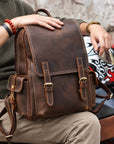 Vintage brown leather backpack for men with buckle straps, top handle and side pockets, front lifestyle view