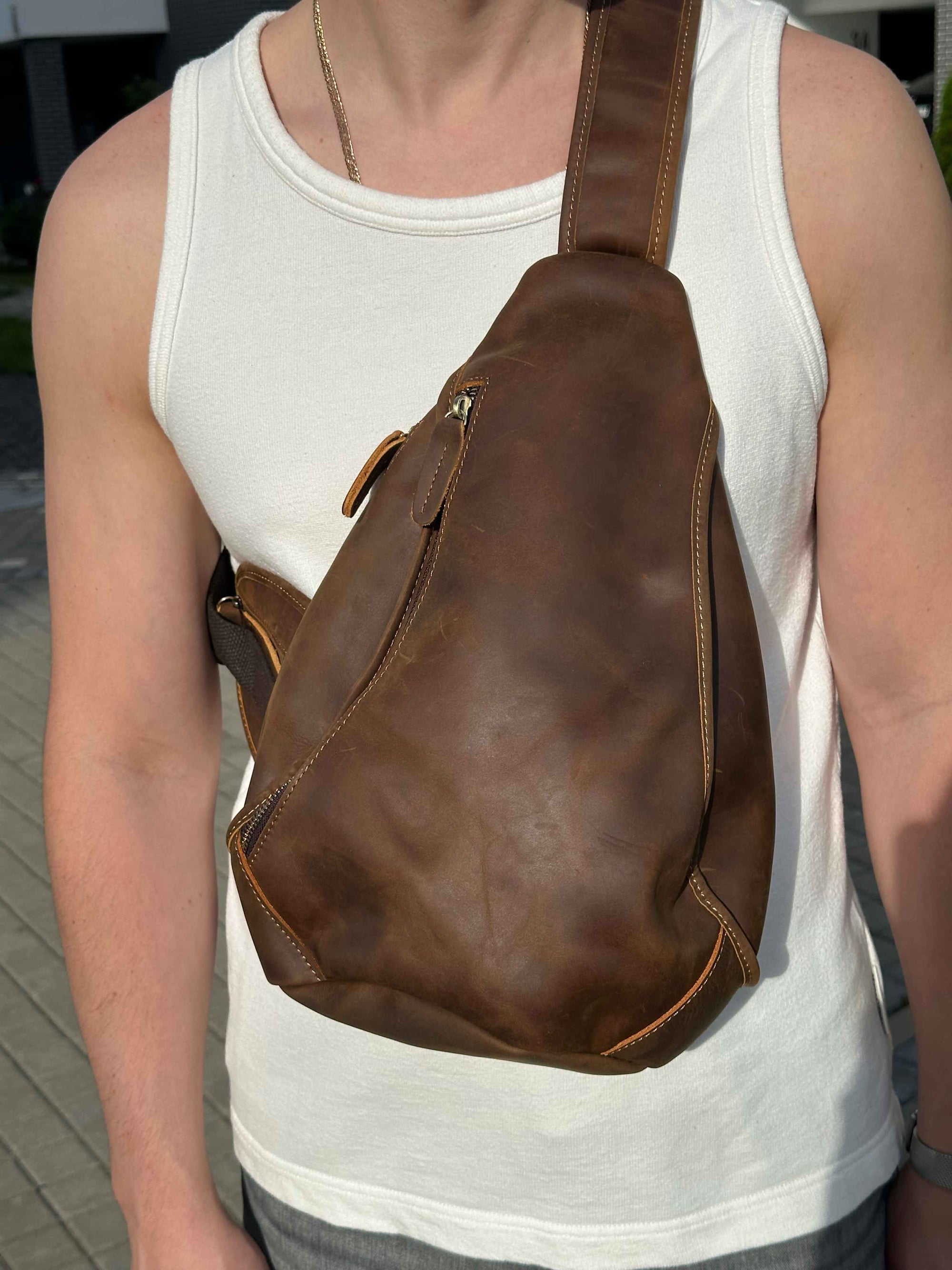 Person wearing a brown leather sling bag over one shoulder.
