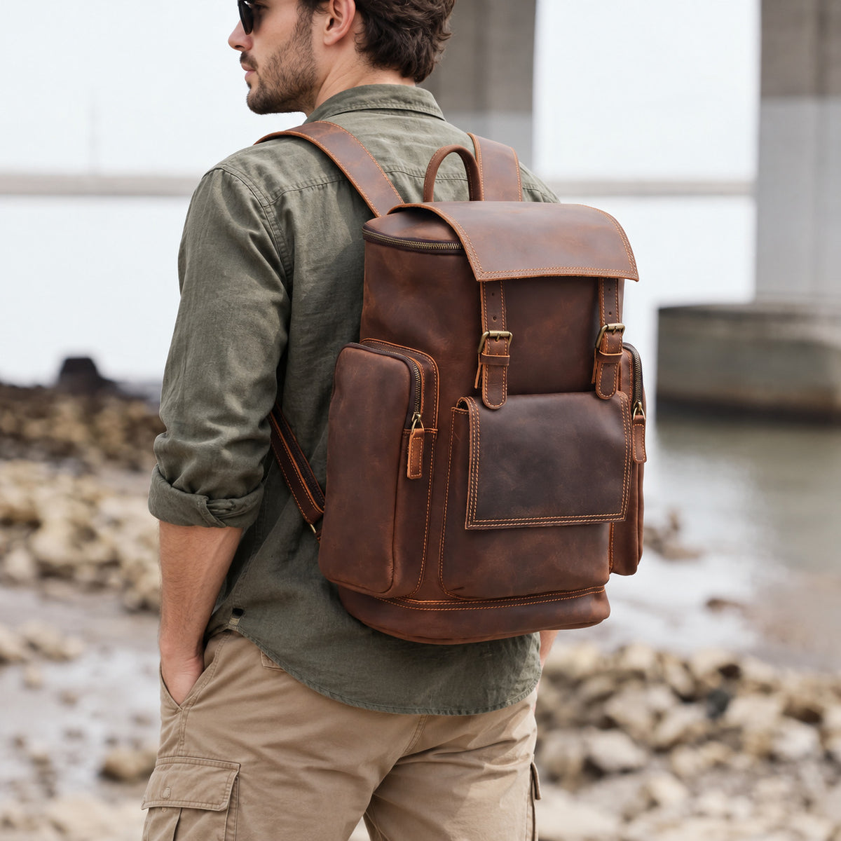 Vintage brown leather travel backpack for men with buckle flap, multiple exterior pockets and adjustable shoulder straps, worn outdoors