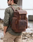 Vintage brown leather travel backpack for men with buckle flap, multiple exterior pockets and adjustable shoulder straps, worn outdoors