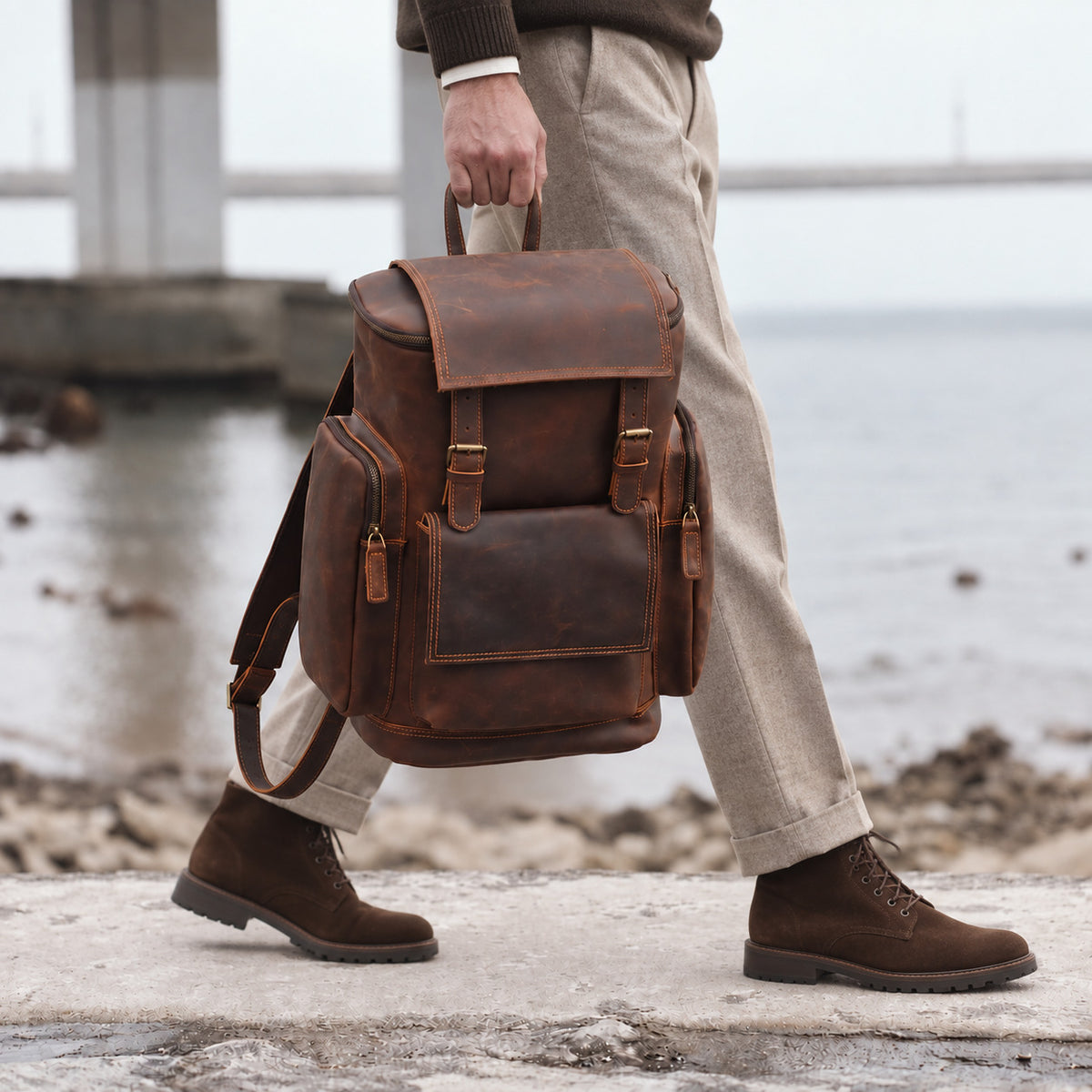 Vintage brown leather travel rucksack for men with multiple pockets, buckle straps and top handle, carried by hand