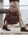 Vintage brown leather travel rucksack for men with multiple pockets, buckle straps and top handle, carried by hand