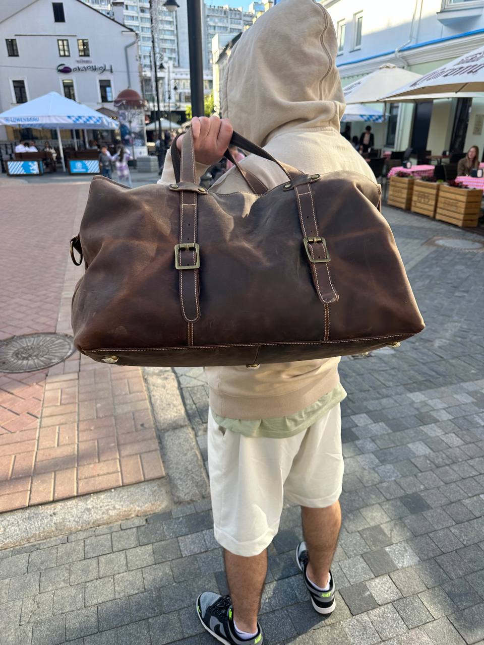 Brown leather duffle bag held in hand, offering a compact and stylish design for both travel and daily use.