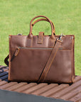 Back view of slim brown men's vintage leather work bag with detachable strap and back zipper pocket on a wooden bench.