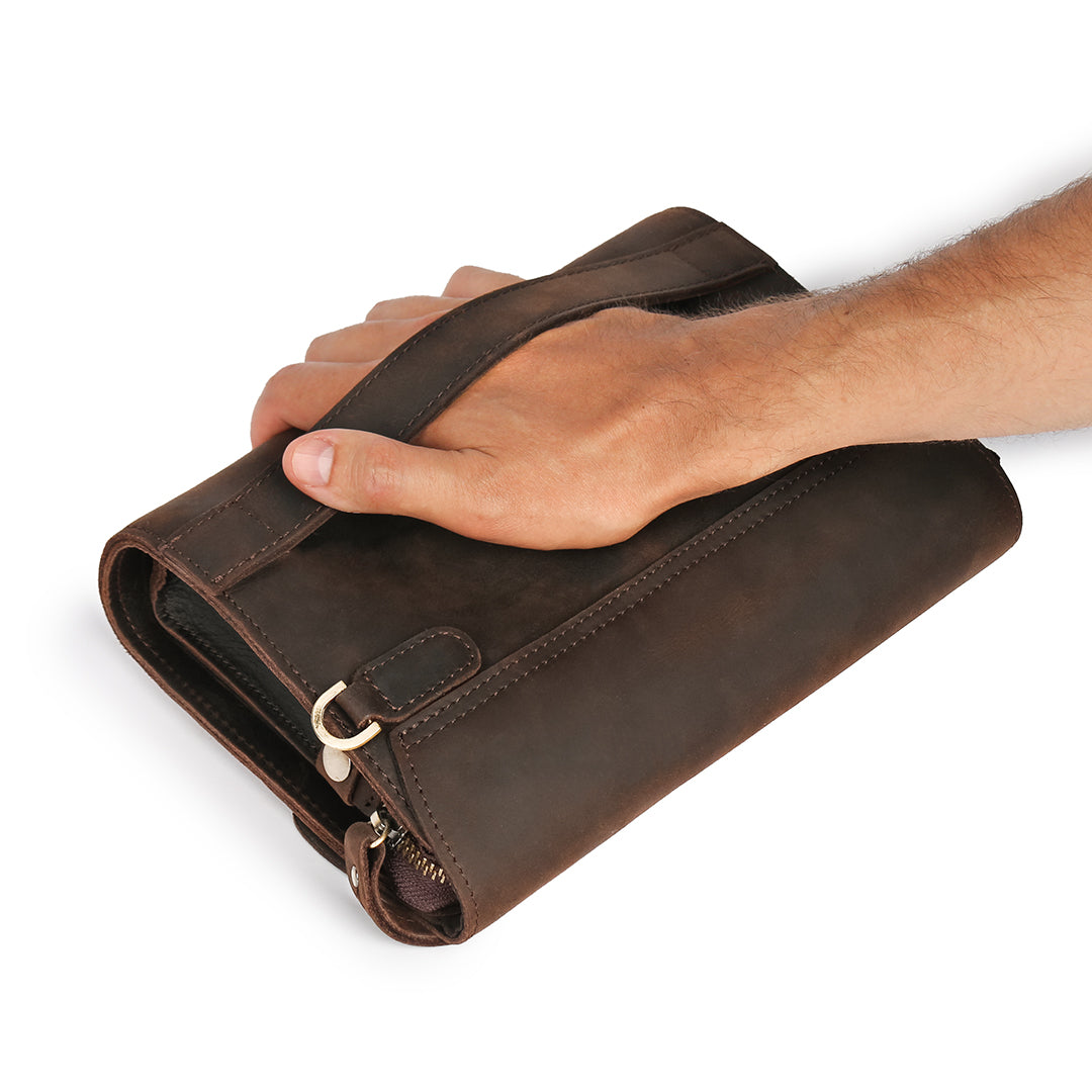 Hand gripping the back strap of a men&#39;s dark brown leather wrist bag, highlighting its comfort and secure design.